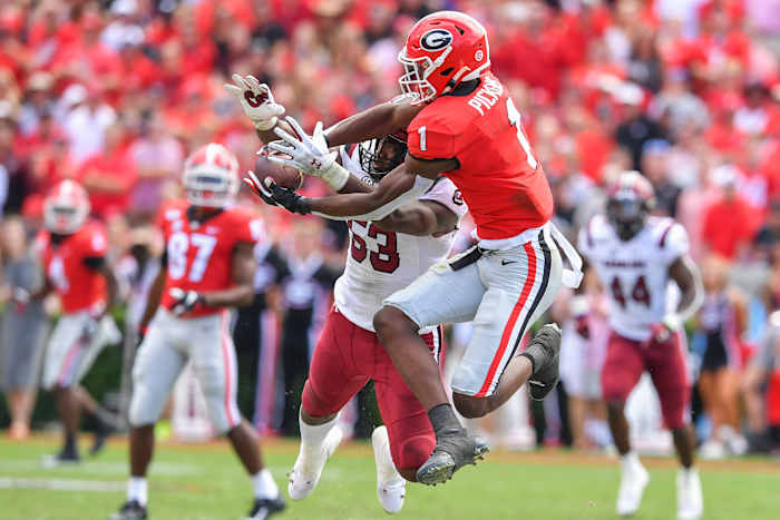Wearing a Georgia Bulldogs uniform, George Pickens jumps to try to catch a ball as a South Carolina defender tries to block it